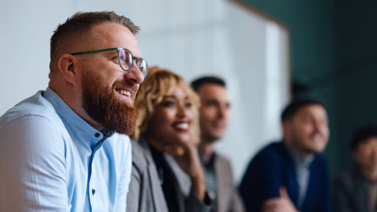 Smiling businessman and unrecognizable multi-ethnic employees sitting in a row at their company desk and listening to their boss.