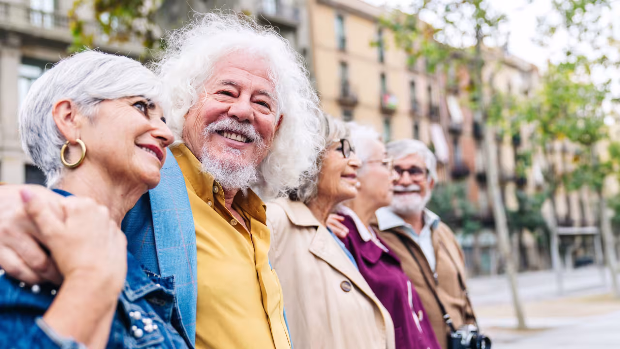 A group of retirees stand in a line posing for a picture on a sightseeing trip in a city. 